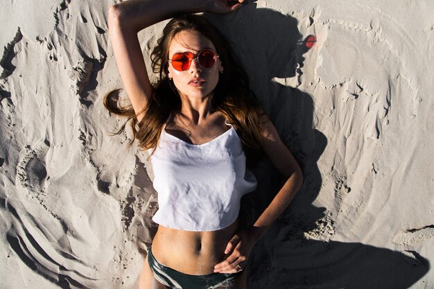 Woman in red sunglasses lies on a white beach