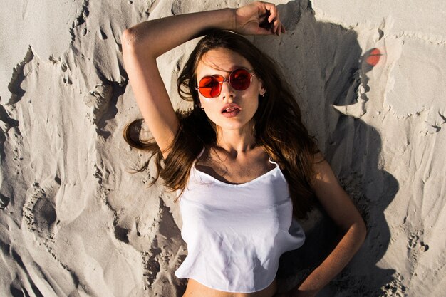 Woman in red sunglasses lies on a white beach