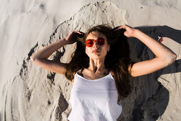 Woman in red sunglasses lies on a white beach