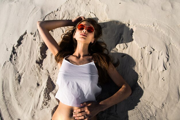 Woman in red sunglasses lies on a white beach