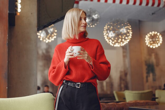 Woman in a red sweater. Lady drinks a coffee.