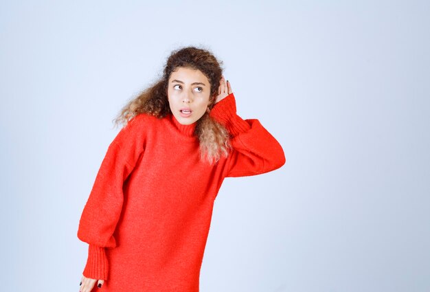 woman in red sweatshirt pointing her hear to listen well.