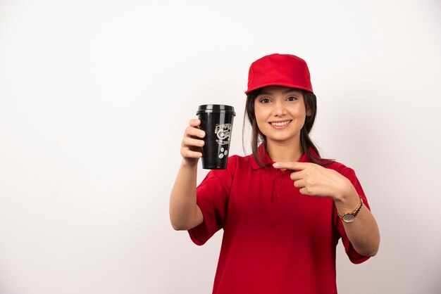 Woman in red uniform showing a cup of coffee on white background.