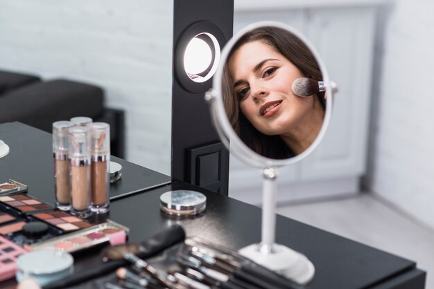 Woman reflecting mirror and applying makeup with brush 