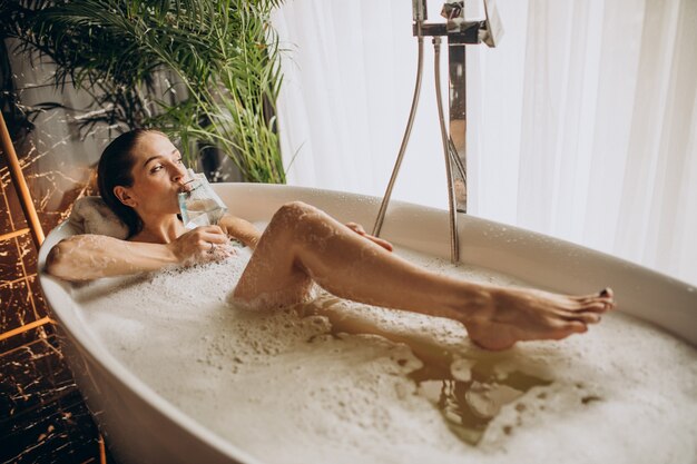 Женщина расслабляется в ванне с пузырьками и пьет вино