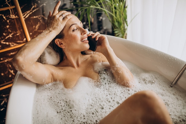 Woman relaxing in bath with bubbles and talking on the phone