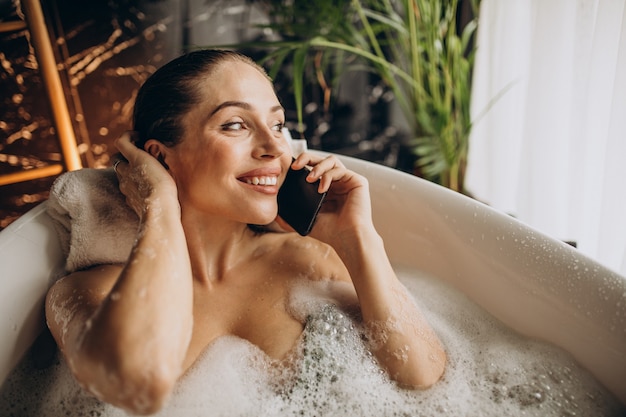 Woman relaxing in bath with bubbles and talking on the phone