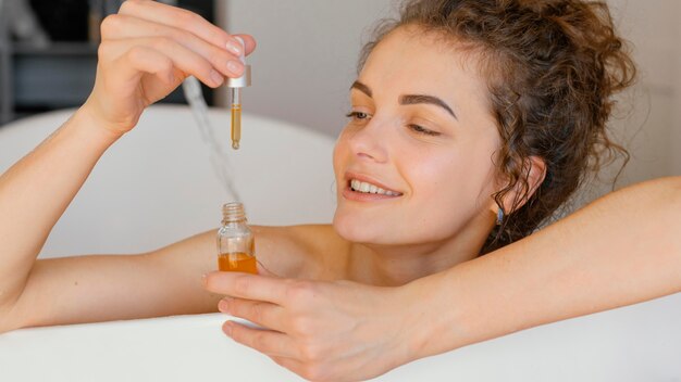 Woman relaxing in bathtub with serum