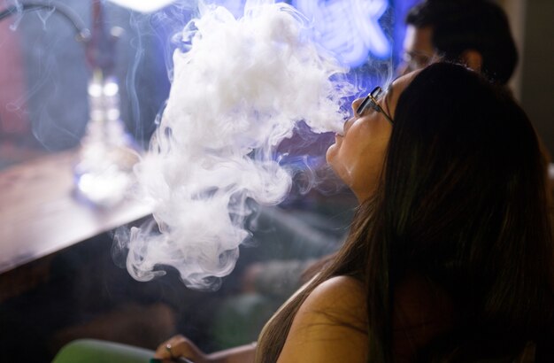Woman relaxing by vaping from a hookah in a bar