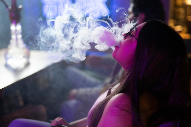 Woman relaxing by vaping from a hookah in a bar