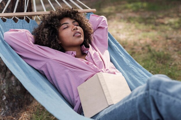 Woman relaxing in hammock while camping outdoors with book