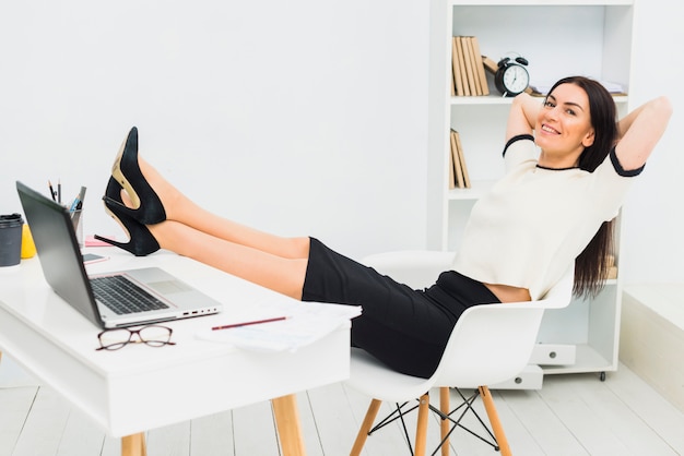 Женщина расслабляющий положить ноги на стол в офисе