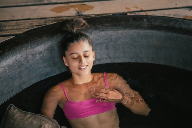 Foto gratuita donna che si rilassa nella cura della pelle organica del bagno all'aperto rotondo nel bagno caldo