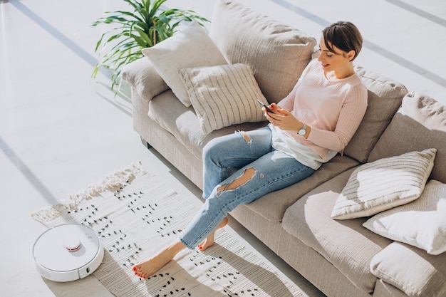 Woman relaxing on sofa while robot vacuum cleaner doing housework