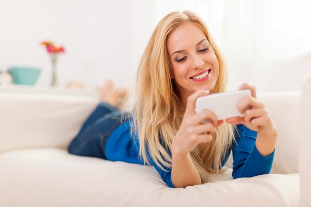 Женщина расслабляется на диване с мобильным телефоном