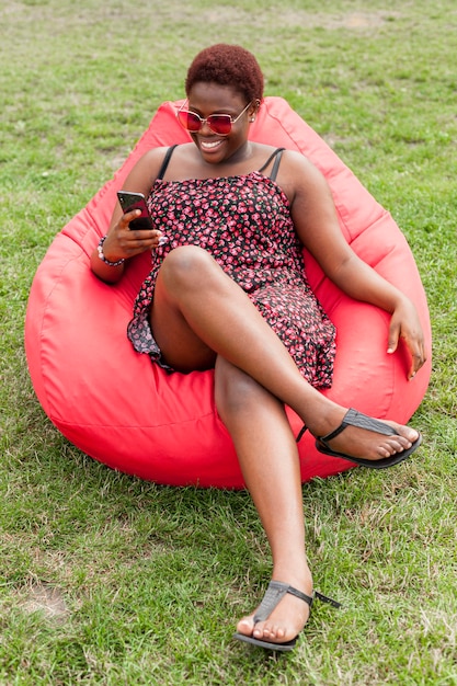 Free photo woman relaxing with smartphone on bean bag outdoors