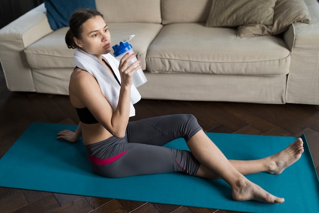Woman relaxing on yoga mat while drinking water