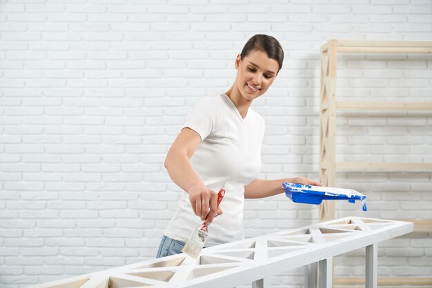 Woman repairing wooden rack using white color and brush