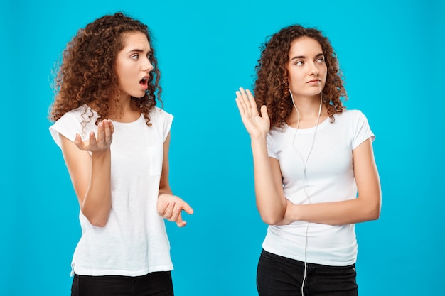 woman resenting at her sister twin in headphones over blue.