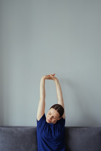 Woman resting on the couch in the living room and stretching her arms