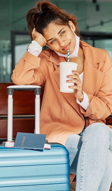 Foto gratuita donna che riposa sui suoi bagagli all'aeroporto e che beve caffè durante la pandemia