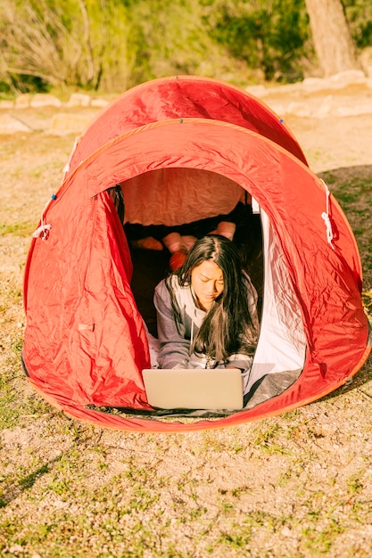 Woman resting in tent and using laptop