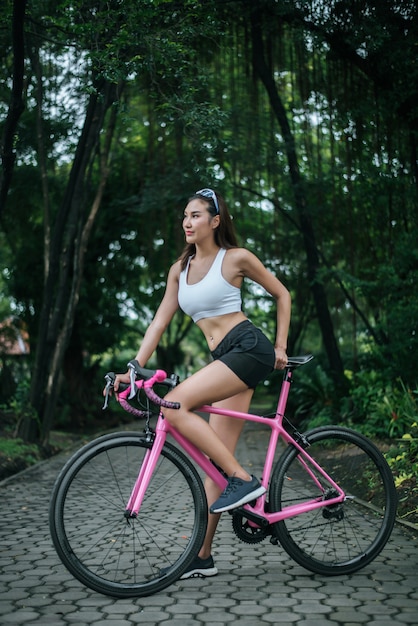 無料写真 公園のロードバイクに乗っている女性。ピンクのバイクで若い美しい女性の肖像画。