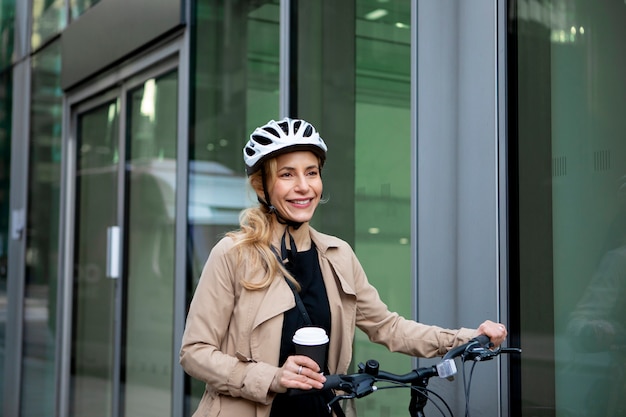 ヘルメットをかぶり、コーヒーを飲みながら自転車に乗る女性
