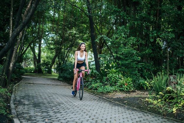 公園のロードバイクに乗っている女性。ピンクのバイクで若い美しい女性の肖像画。