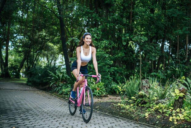 Женщина верхом на велосипеде в парке. Портрет молодой красивой женщины на розовый велосипед.