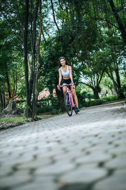 공원에서 자전거를 타는 여자. 핑크 자전거에 아름 다운 젊은 여자의 초상화입니다.