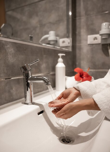 A woman in a robe washes her hands under running water from a tap.