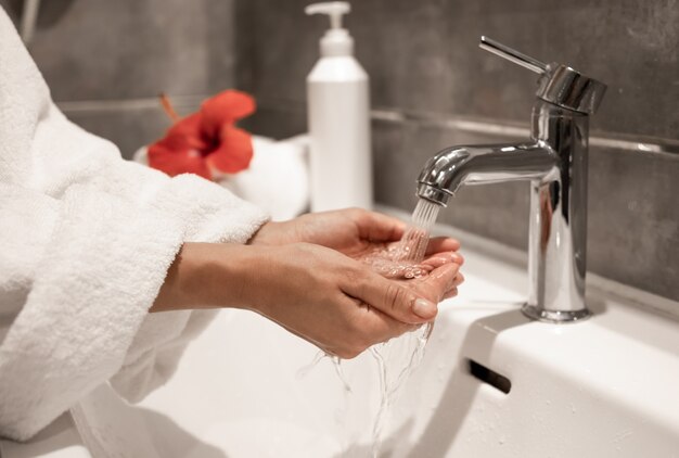 A woman in a robe washes her hands under running water from a tap