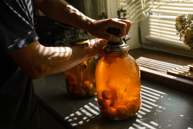 Free photo a woman rolls a compote in a large jar under the sun in summer at home in the village