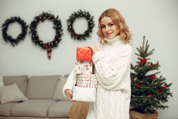 Donna in una stanza. bionda con un maglione bianco. signora vicino all'albero di natale.