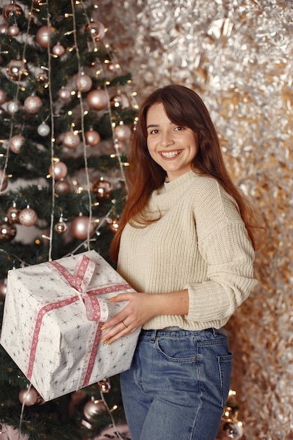 Woman in a room. Girl in a white sweater. Lady near christmas tree.