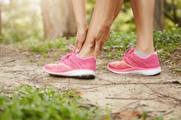 Woman runner holding her twisted ankle after running exercise outdoors.