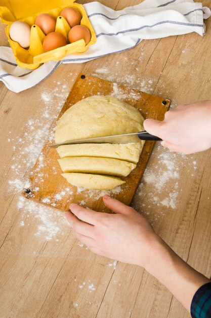 A woman's hand cutting the dough with knife for preparing italian gnocchi pasta on wooden desk