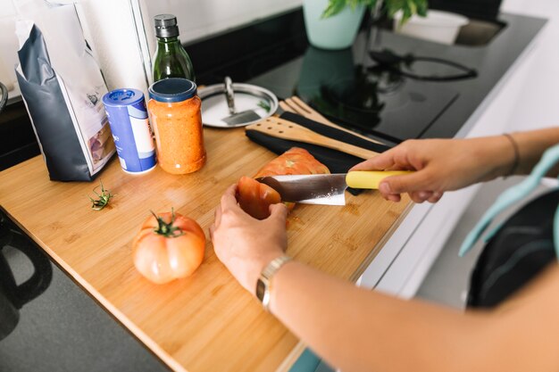 부엌 카운터에 칼으로 토마토의 여자의 손 절단 조각