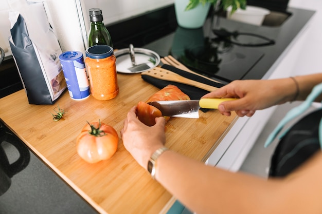 Woman's hand cutting slices of tomato with knife on kitchen counter