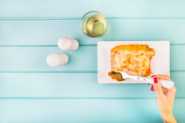 Le mani della donna che mangiano lasagne su fondo di legno