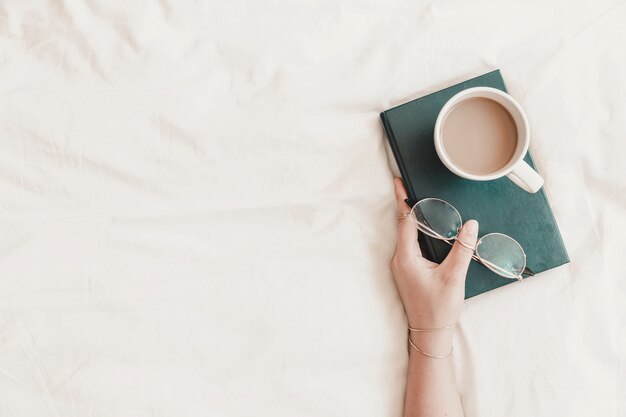 Woman's hand holding book with eyeglasses and hot drink on it