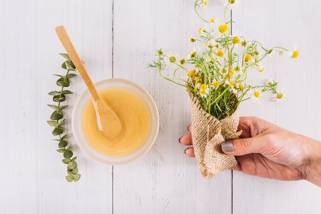 Foto gratuita la mano della donna che tiene il mazzo di fiori della camomilla vicino alla ciotola di cagliata di limone