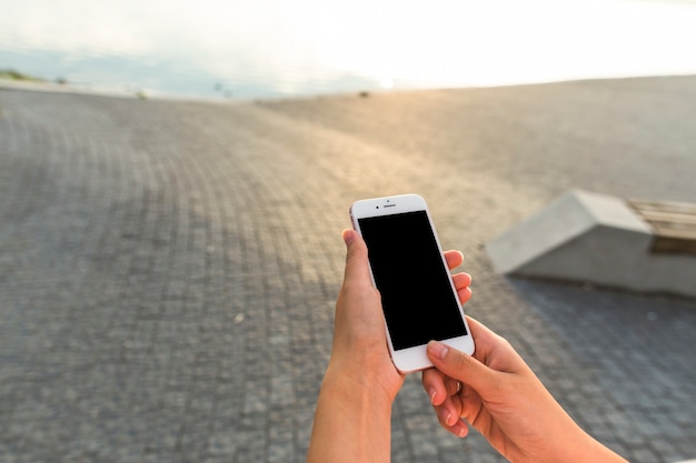 Free photo woman's hand holding cellphone at outdoors