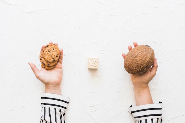 Free photo woman's hand holding cookies versus coconut over white textured backdrop