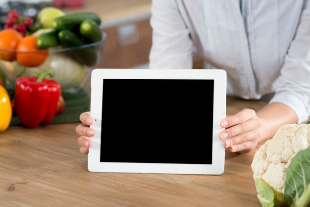 woman's hand holding digital tablet with blank screen on wooden kitchen counter