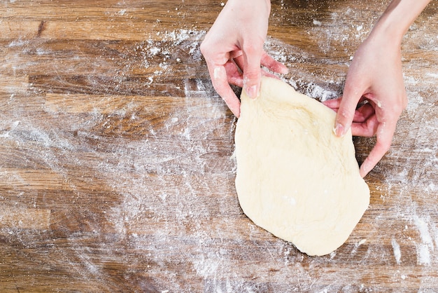 Free photo woman's hand holding flattened dough over the wooden desk