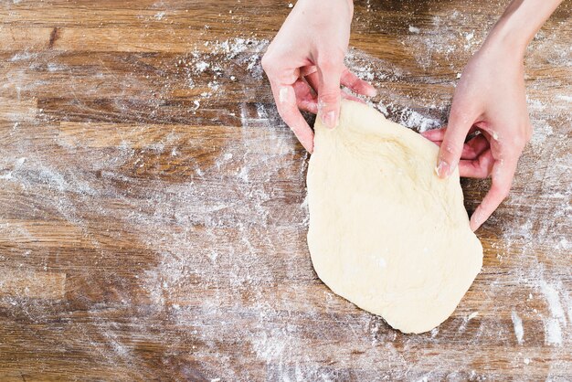Woman's hand holding flattened dough over the wooden desk