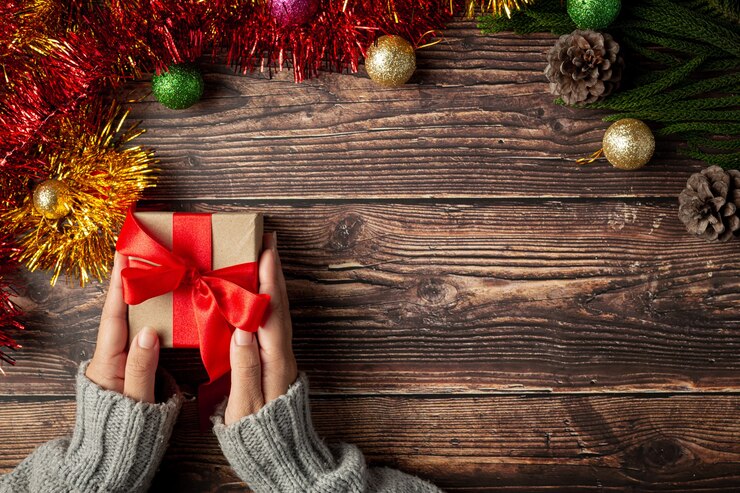 Free Photo woman's hand holding a gift box with red ribbon on wooden floor