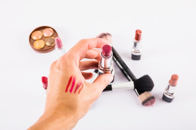 Woman's hand holding lipstick with brushes on white surface